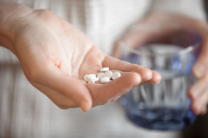 Womans Hands Holding Heap Of White Round Pills And Glass Of Wate