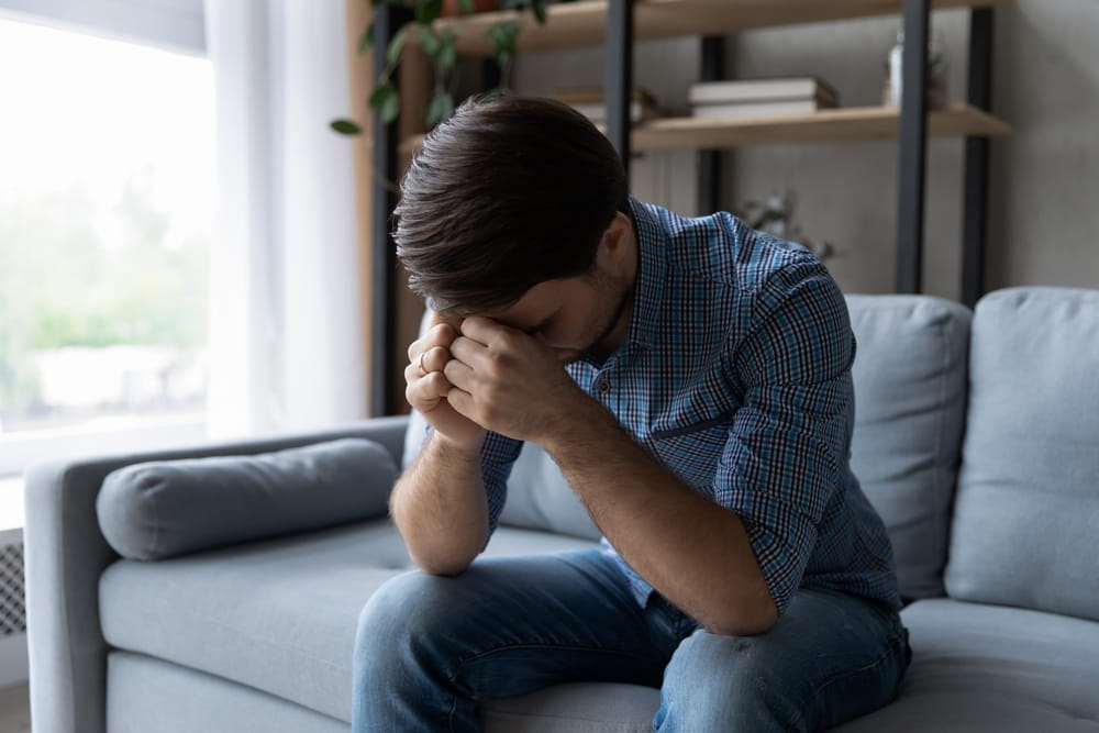 Man sitting on couch holding his head showing emotional distress after a dog attack in Michigan